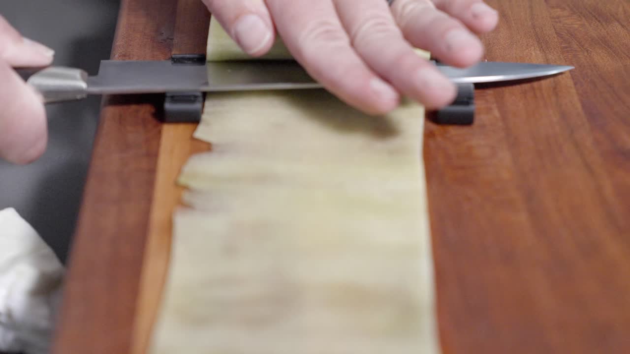 A tracking shot captures a chef peeling and rolling a cucumber on a wooden cutting board, filmed at 120 fps to highlight smooth motion and precision. Ideal for culinary and food preparation content.