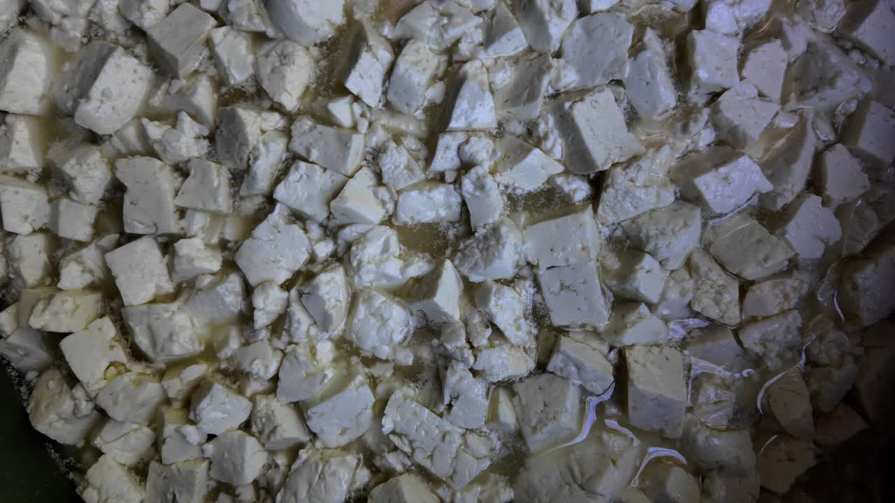 수제 치즈 제조 과정 중 신선한 치즈 커드가 유청에 잠겨 있는 섬세한 텍스처를 포착한 제니스 숏이에요.