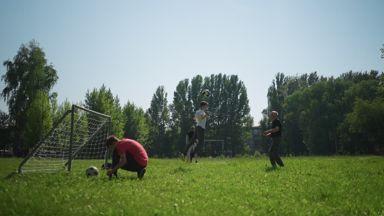 A grandfather and grandson are playing football outdoors as the grandfather throws the ball and the grandson heads the ball high as the grandfather move to get the ball