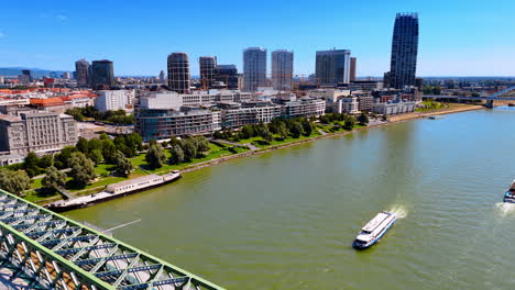riverboat goes towards the old bridge crossing the danube. modern skyline of bratislava, slovakia. aerial view