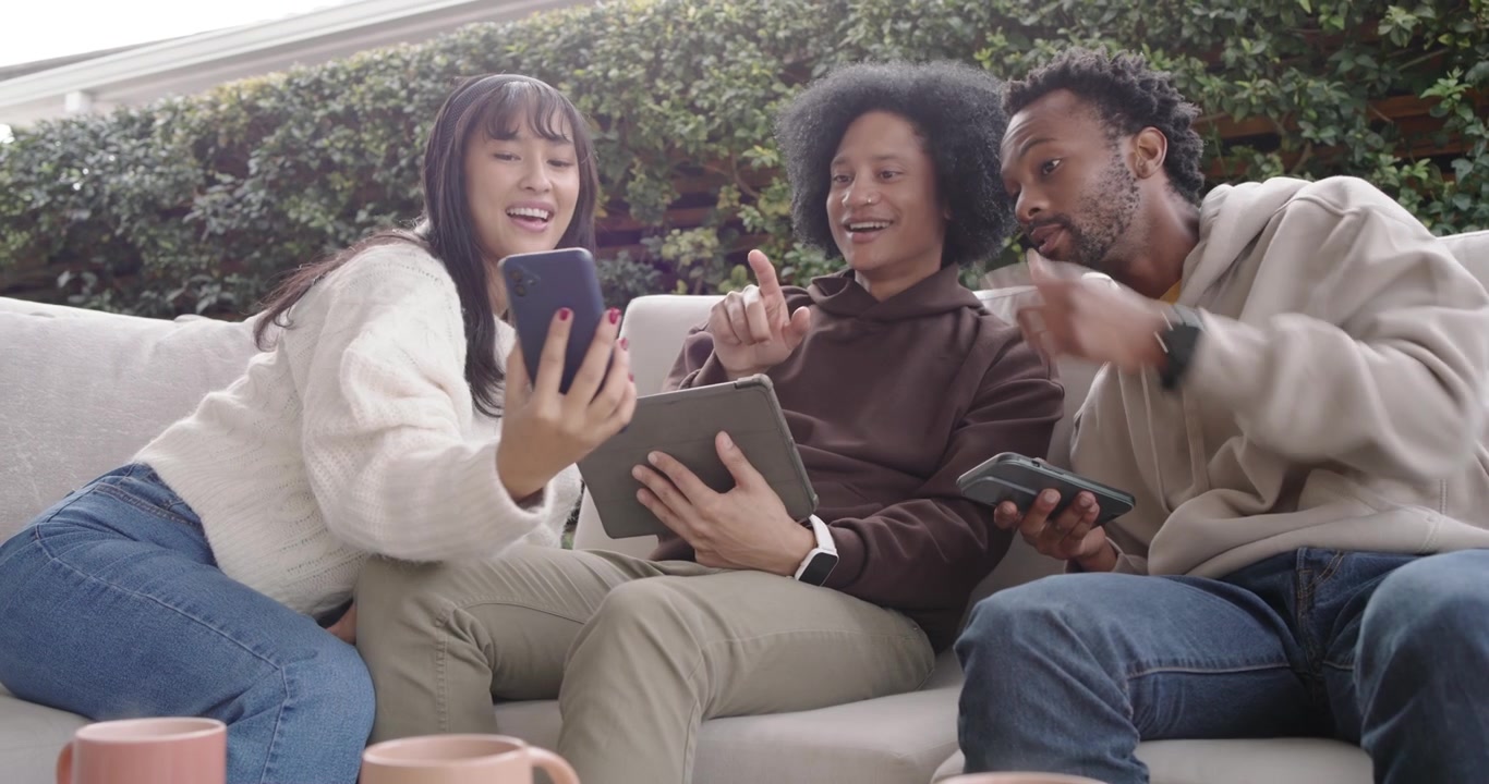 African American friends sitting on patio sofa left woman handing phone for viewing tablet