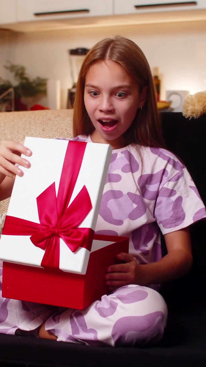 Ragazza adolescente apre una confezione regalo, sorpresa gioiosa, vede il giocattolo desiderato all'interno, sorride con reazione eccitata e un grande sorriso.