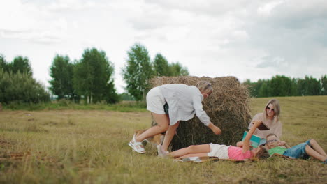 la madre entrega el libro a la hija mientras la niña lo pasa al hermano, la tía se sienta cerca mientras la abuela está con el perro en un entorno de granja sereno, rodeada de naturaleza