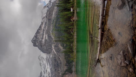 vertical 4k timelapse, dramatic clouds moving above snow capped peaks and crystal clear lake water