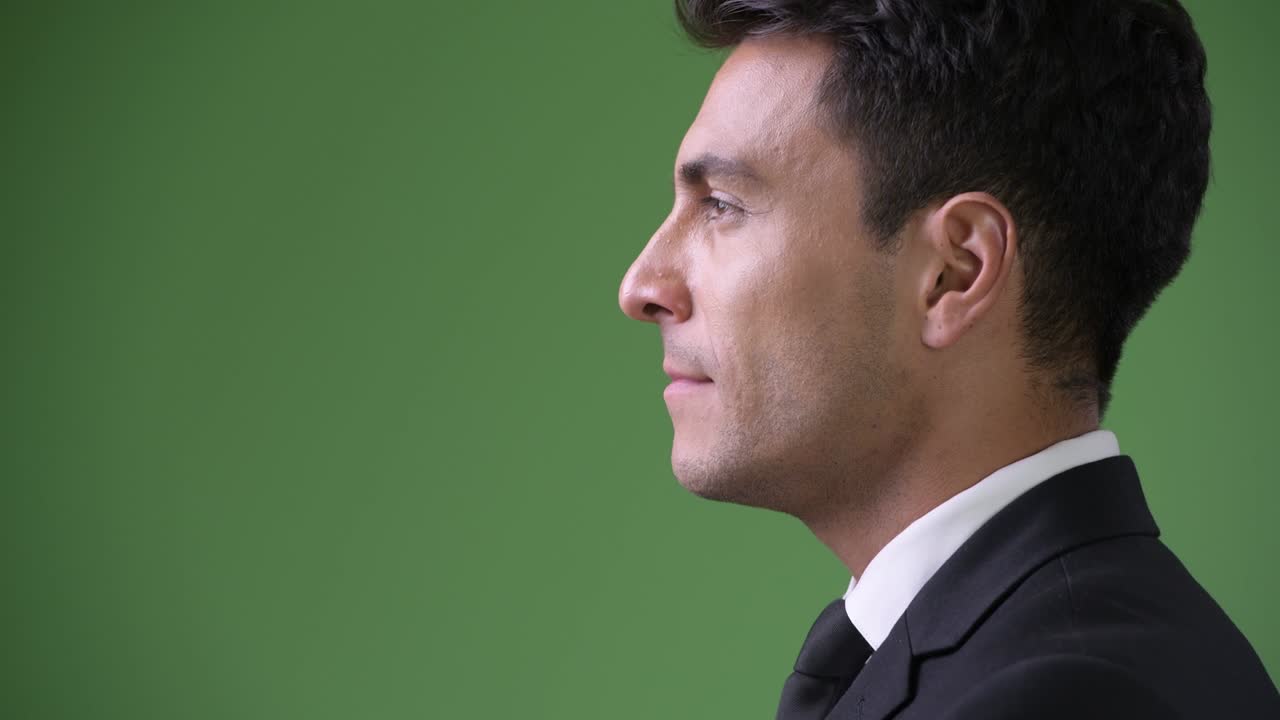 Young handsome Hispanic businessman against green background