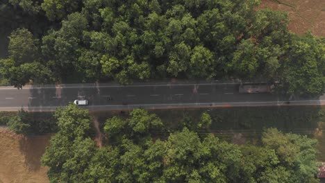 Von-Oben-Nach-Unten-4K-Luftaufnahme-Von-Autos,-Die-An-Einer-Von-Wald-Umgebenen-Landstraße-Vorbeifahren