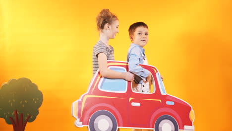 happy children with a big toy car on a bright yellow wall background. children's scenery in the studio