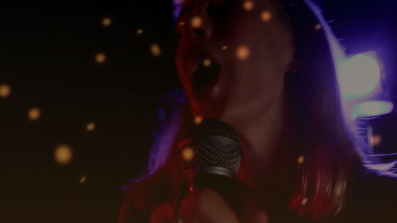Female singer performing with microphone on music stage, with floating orange bokeh light particles