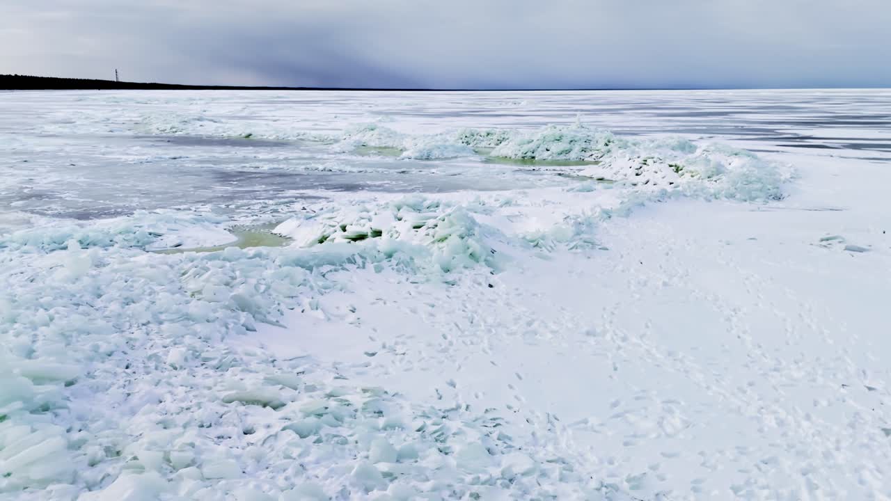 Toma de dron sobre la costa congelada, crestas de presión con torres de hielo hechas a mano y losas rotas, mostrando patrones de paisajes invernales, nieve acumulada y peligrosos charcos de deshielo