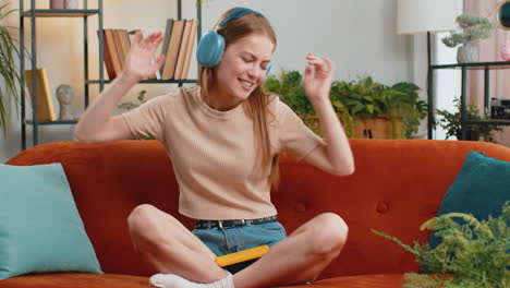 happy young woman in wireless headphones relaxing lying on sofa at home listening favorite music