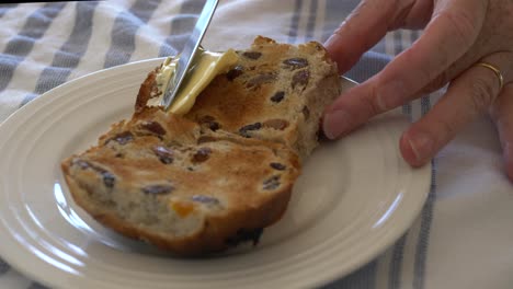 Sartén-A-Cámara-Lenta-En-Bollos-Cruzados-Calientes-Recién-Cocinados-Que-Se-Untan-Con-Mantequilla-En-Un-Plato-Blanco-Durante-La-Pascua