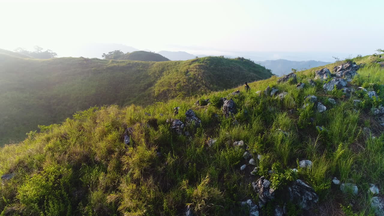산 꼭대기에 있는 큰 바위를 지나가는 여성 등산객의 공중 궤도 샷