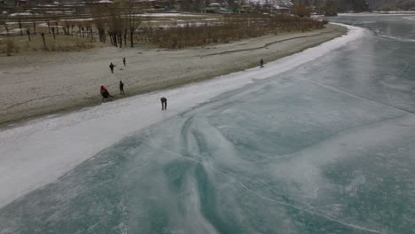 aerial view over silhouette of people ice skating on frozen khalti lake at ghizer valley