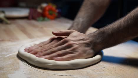 a close-up of a skilled chef's hands pressing and shallowing pizza dough on the wooden counter