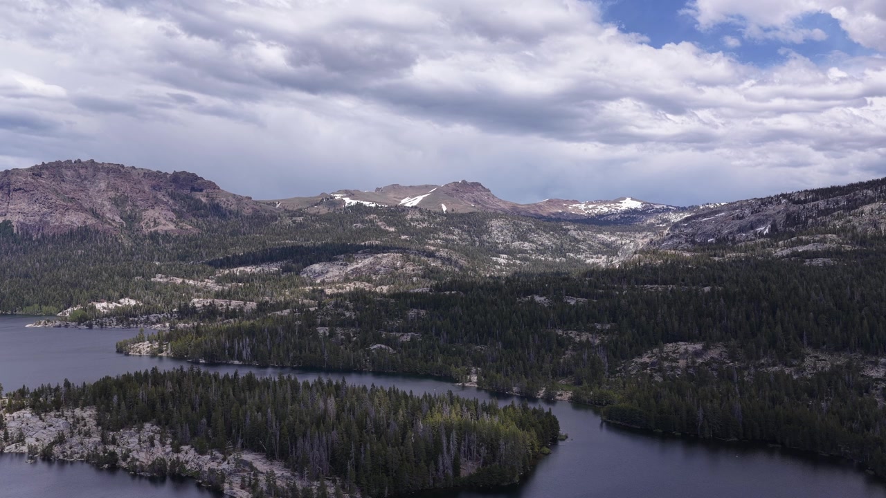 Inquadratura statica del Silver Lake in California, che mostra la costa boscosa e le aspre montagne innevate della Sierra Nevada sotto un cielo drammatico e nuvoloso