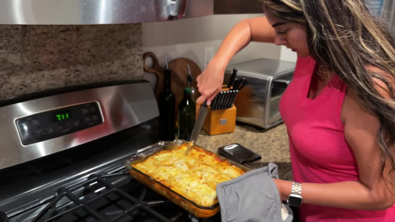 joven mujer hispana cortando lasaña terminada en la cocina lista para la cena