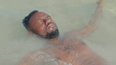 a bare-chested black man falls backward into the ocean and enjoys the water