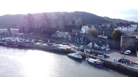 idyllic conwy castle and harbour fishing town boats on coastal shimmering waterfront aerial slow push in