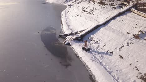 dron descendiendo cerca de la orilla del lago congelado con un hombre secándose con una toalla después de nadar en el hielo