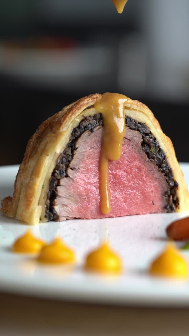 Uno chef versa la salsa su fette di Beef Wellington, primo piano, inquadratura di inserto