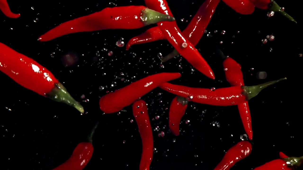Peperoncini rossi che cadono e schizzano nell'acqua su sfondo nero.