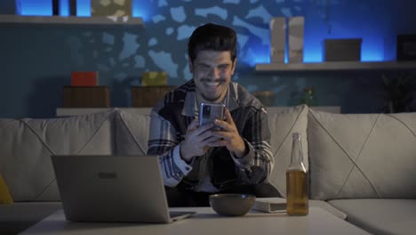joven feliz en casa hablando por teléfono y bebiendo alcohol.