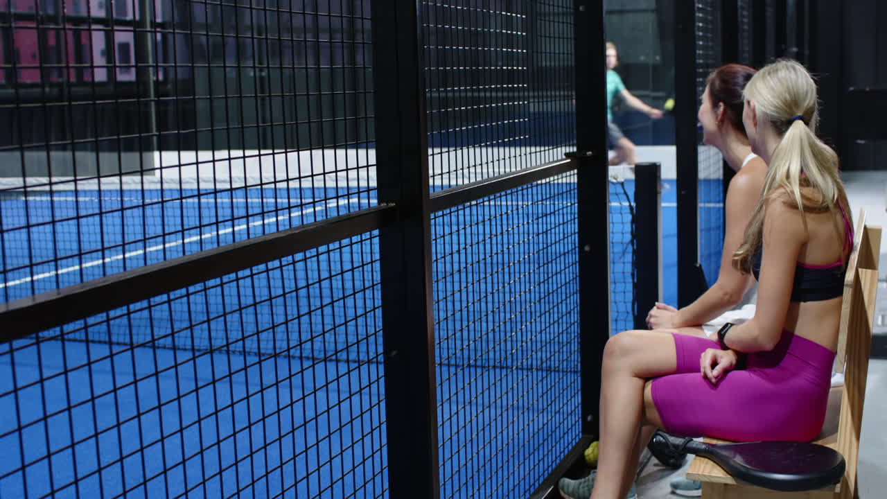 Woman in pink sportswear resting on bench watching padel tennis match, on indoor court
