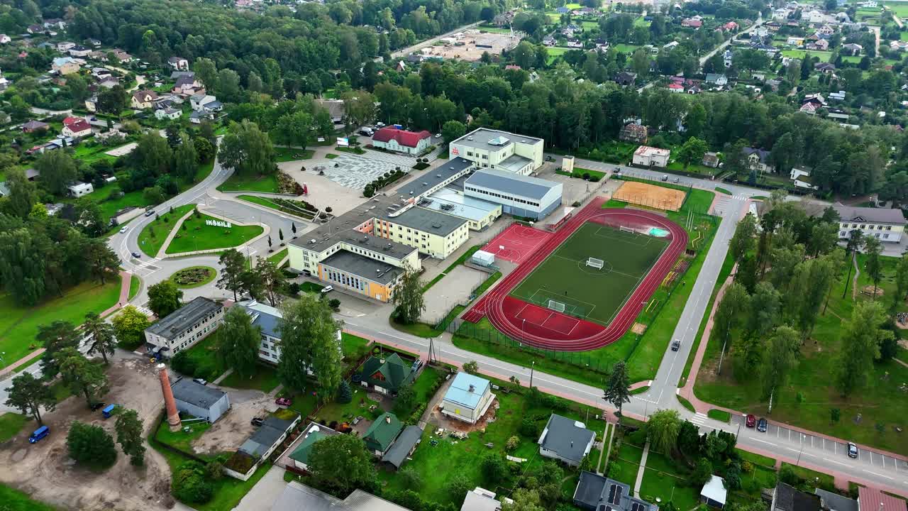 Drone view of Ikskile, Latvia, featuring the secondary comprehensive school complex with track and field, municipal cultural centre with town’s peaceful urban and educational landscape