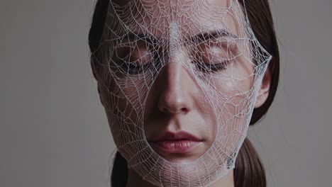 woman wearing translucent spiderweb like veil draping delicately over closed eyes, embodying ethereal femininity with serene, contemplative expression against neutral studio background