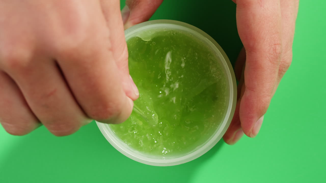 Woman hand stir a Fresh ripe avocados with cream and essential oil on green background with mint mentol, make up cosmetics