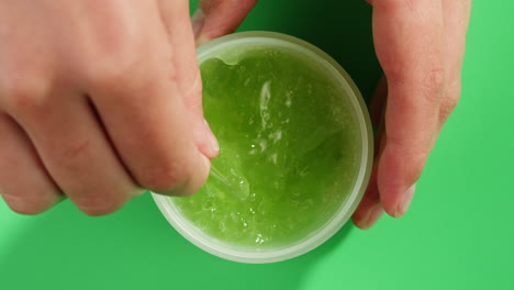 woman hand stir a fresh ripe avocados with cream and essential oil on green background with mint mentol, make up cosmetics