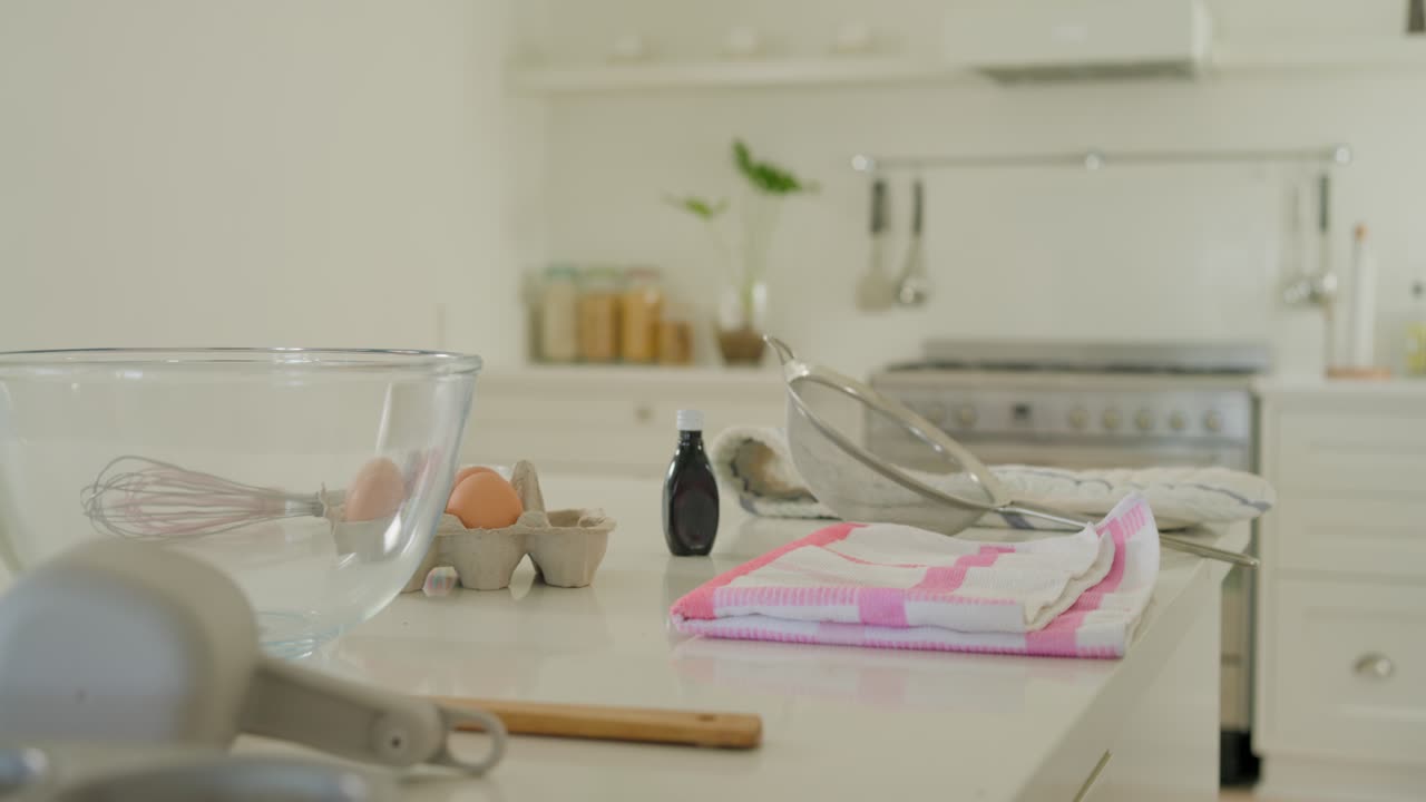 La telecamera scorre a sinistra e indietro, mostrando l'allestimento per la cottura in cucina: ciotola per mescolare, uova, setaccio, postazione di lavoro.