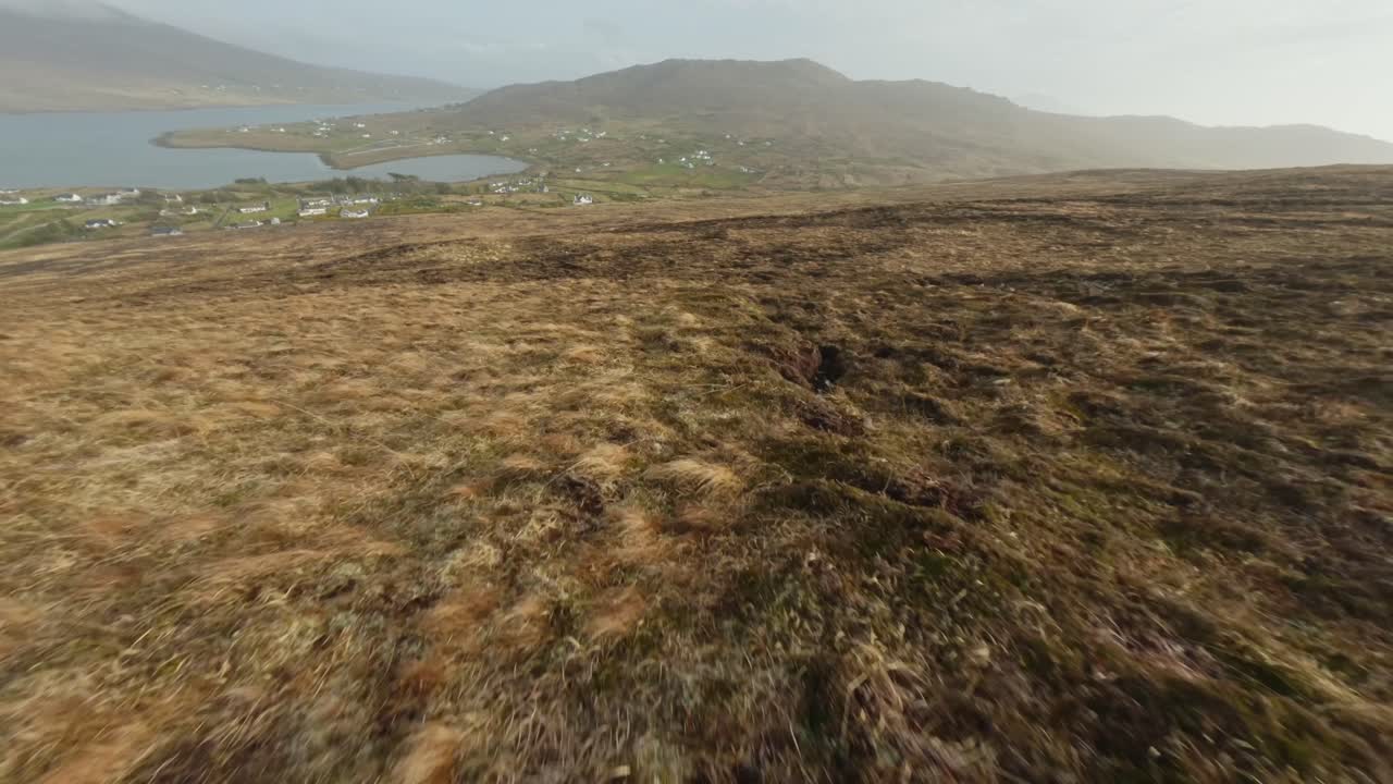 disparo rápido de avión no tripulado volando cuesta abajo hacia un pequeño pueblo en la luz de la tarde, isla de achill
