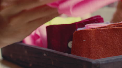person handling colorful felt items in wooden tray