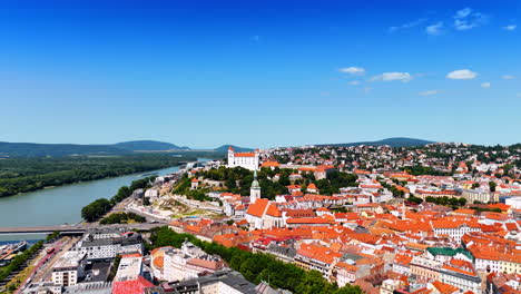 bratislava castle surrounded by the lush greenery towers over the scenery of old town. aerial perspective on the historical part on sunny day