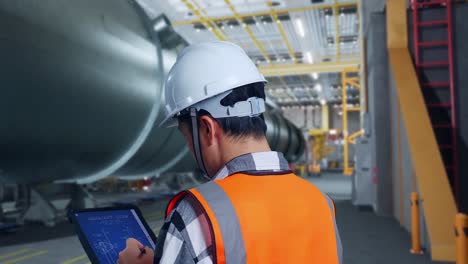 vista de cerca de atrás de un ingeniero masculino asiático con casco de seguridad diseño de turbina eólica plano en una tableta en una fábrica de fabricación de tubos