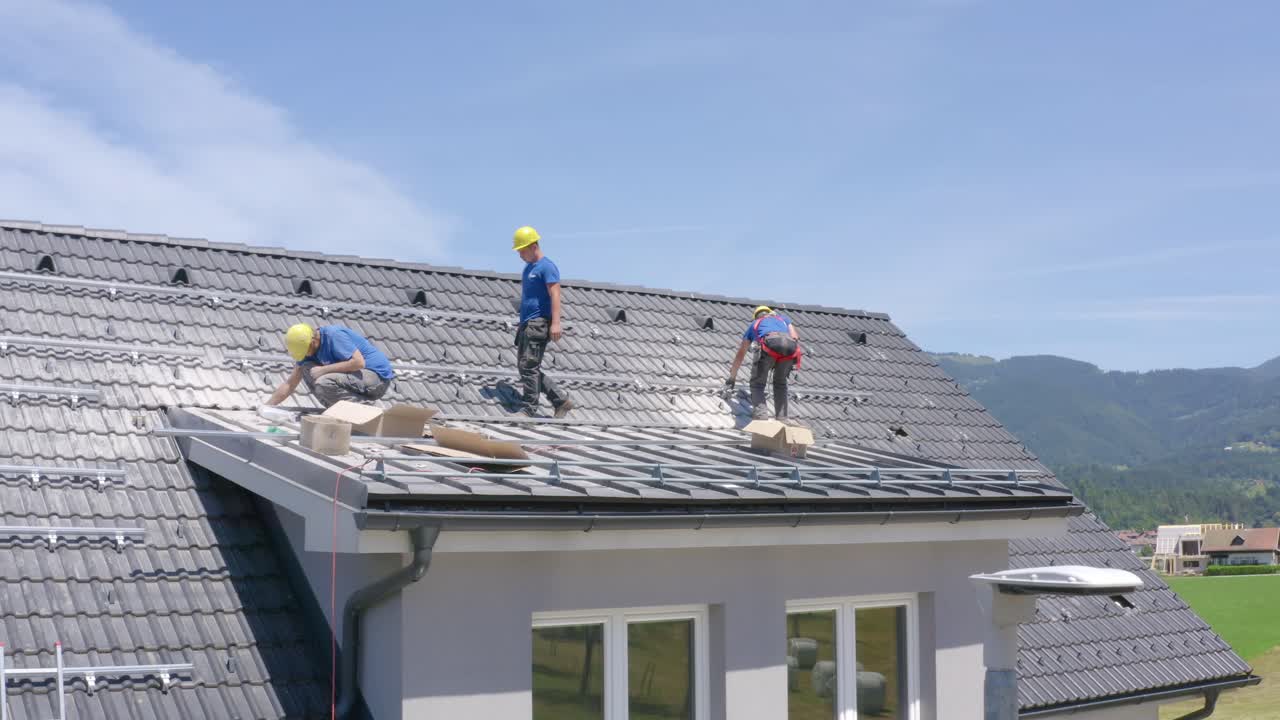 Three men installing solar panels on house roof in Slovenia. Aerial descent