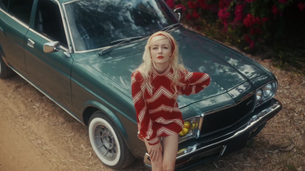 Mujer rubia con estilo posando con un coche verde antiguo en exteriores