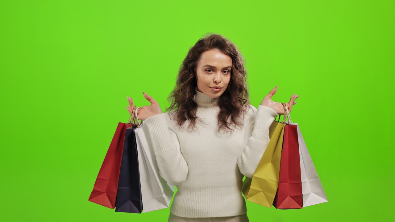 여성은 카메라를 바라보고 있습니다. 그녀는 쇼핑 가방을 집어 들고 있습니다. 그녀는 초록색 배경에 서 있습니다. 초록색 화면.