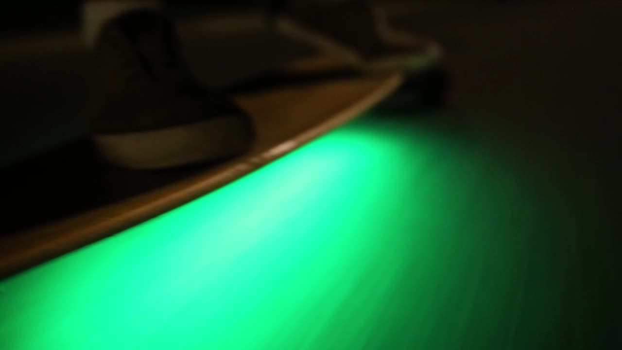 Close up shot of riding skateboard with neon lights. The view of board and wheels. Person standing up