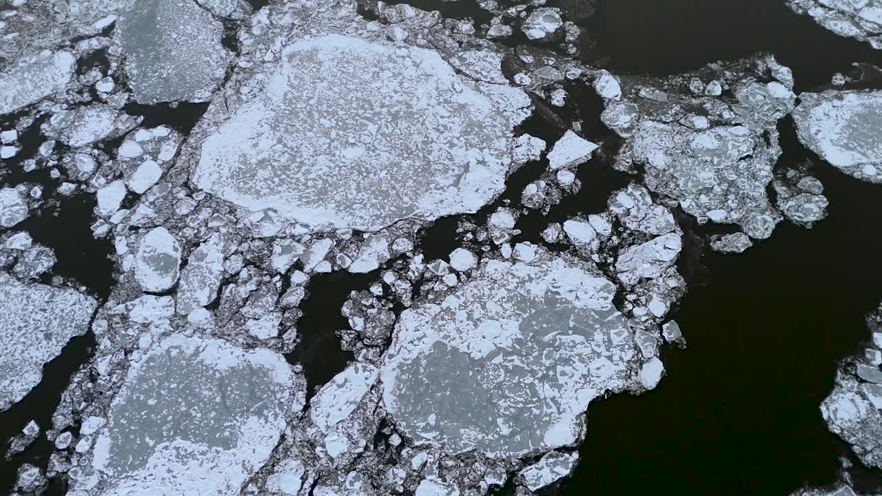 Majestuosa toma aérea de fragmentos de hielo flotando en el río Hudson, rodeados de aguas oscuras. La escena invernal refleja un contraste natural único, mostrando los intrincados patrones formados por t