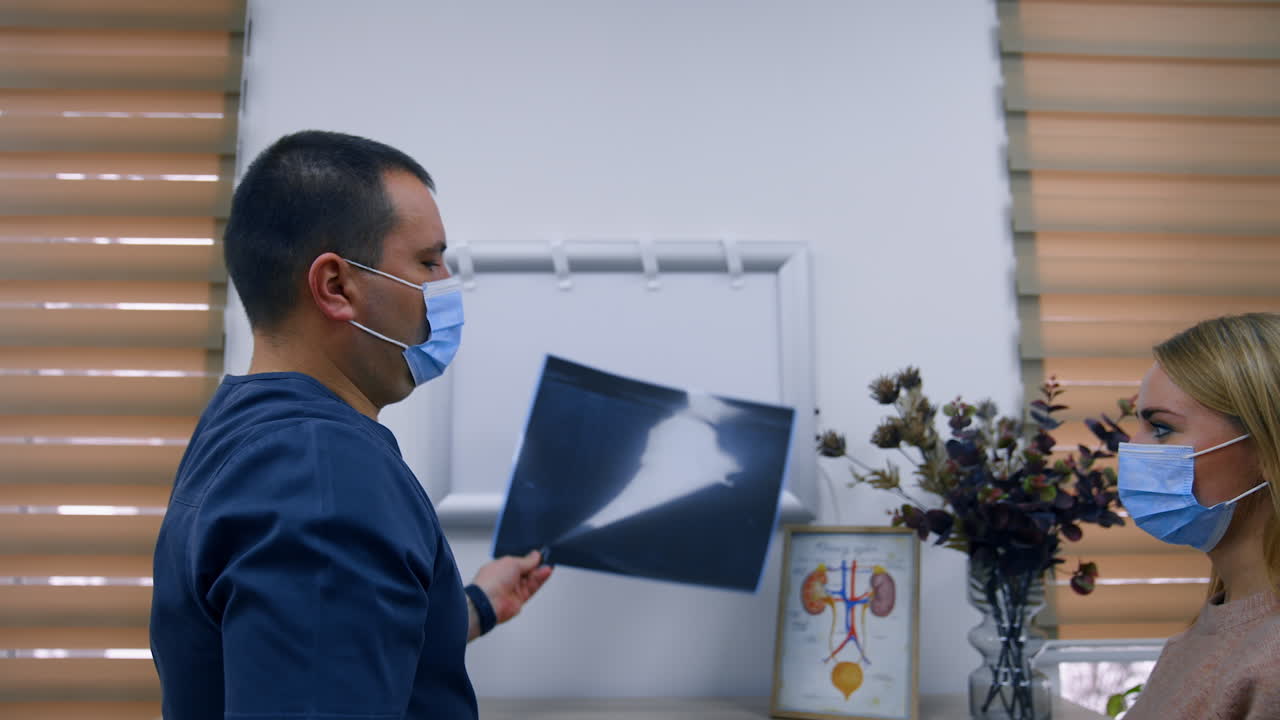 Healthcare specialist switches off the light screen and gives x-ray scan to a patient. Blonde long-haired woman takes the shot and thanks to a doctor.