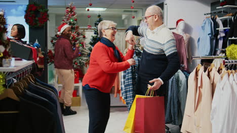 senior man holding shopping bags, spinning wife in festive decorated fashion shop, happy after finding ideal presents to share with family members at christmas event party