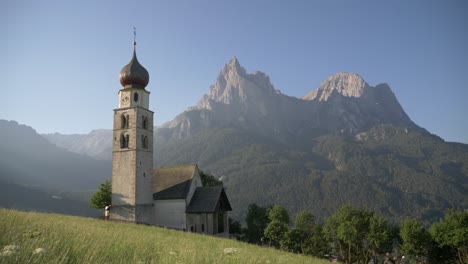 Beautiful-Old-Church-Tower-in-a-valley-with-a-Mountain-Backdrop-in-the-European-Dolimites-French-Alps,-Ortisei