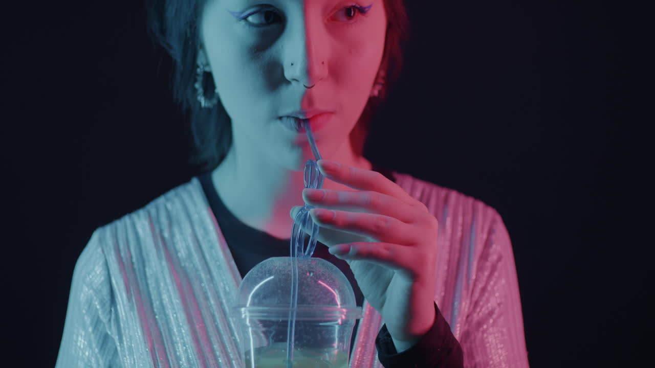 Woman drinking neon drink under colorful lights