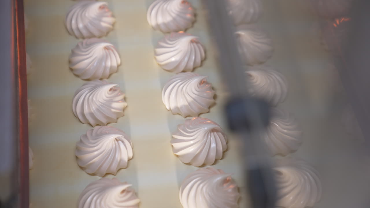 Delicious creamy marshmallow sweets moving slowly on the conveyor belt. Freshly-made vanilla desserts come out from machine. Close up. Top view.