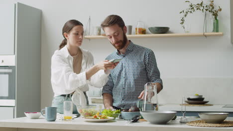 mujer tomando fotos de comida en la mesa en casa, mientras el hombre mira y dice algo divertido