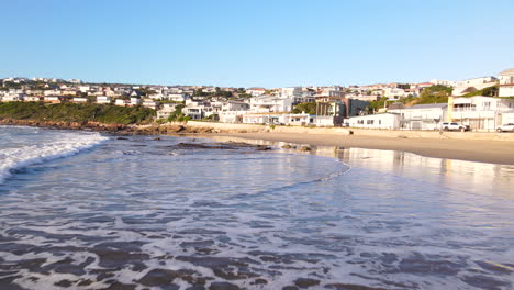 low sunrise aerial pullback over waves running out onto vleesbaai beach village