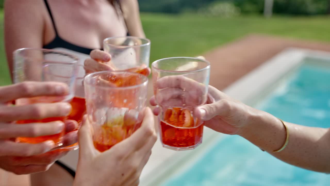 Group of friends cheer and cling glasses of refreshing drink or cocktail by pool in summer vacation outdoors on hot day. Happy and cheerful fun celebration of swimming pool party during holiday