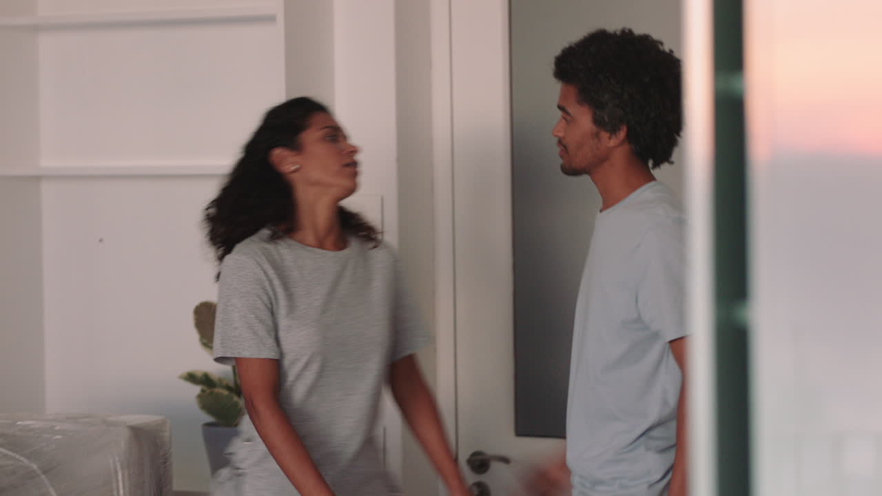 젊은 부부가 집을 옮기고 새로운 주택 소유자들이 미소 짓고 성공적인 이사를 즐기며 아파트에서 포옹하고 있습니다.